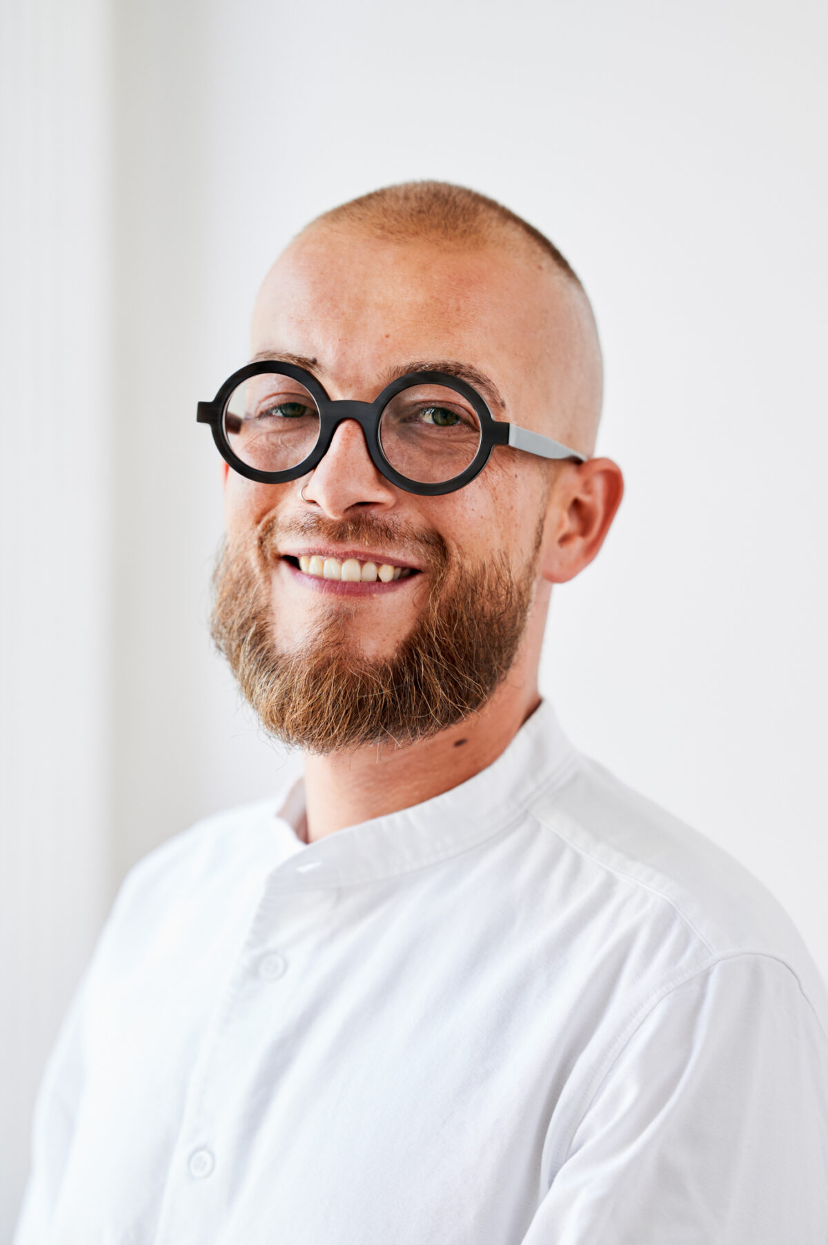 Ein lächelnder Mann mit Brille und weißem Hemd.
