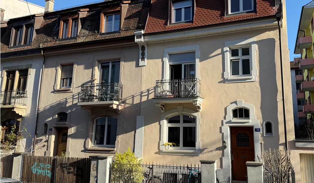 Ein helles Mehrfamilienhaus mit Balkonen und einem Holztor.