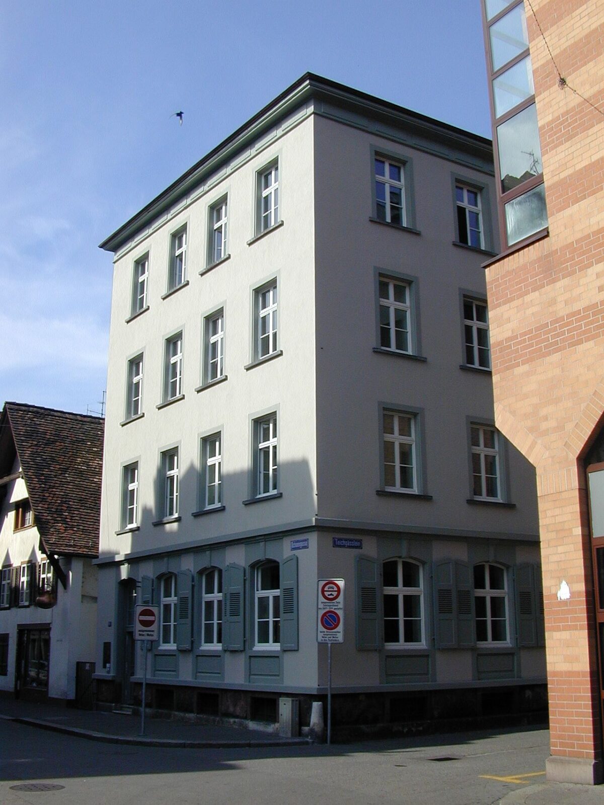 Ein weißes Mehrfamilienhaus an einer Straßenecke mit mehreren Fenstern.