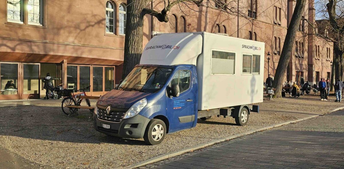 Ein blauer und weißer Sprachmobil-Wagen steht vor einem Gebäude.
