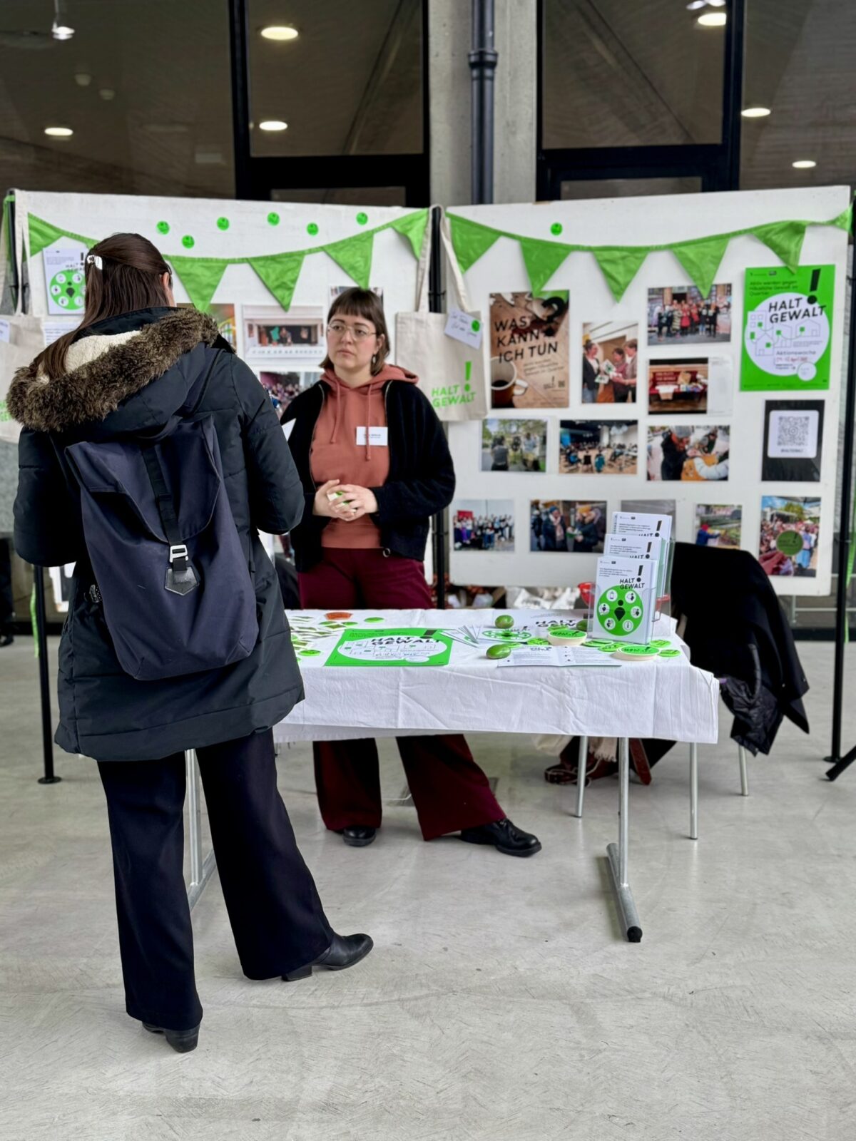 Halt Gewalt Zwei Personen stehen an einem Informationsstand mit Plakaten und Materialien zum Thema Gewaltprävention.