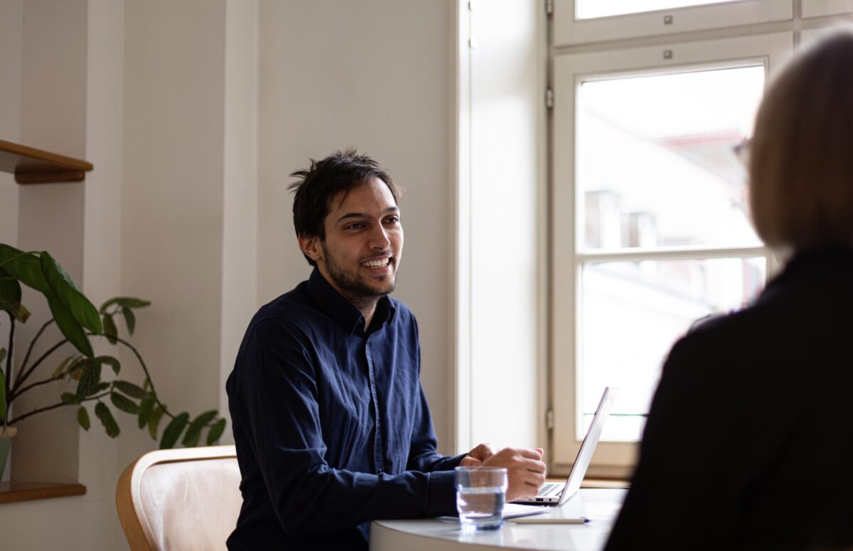 Caritas beider Basel Zwei Personen sitzen an einem Tisch und unterhalten sich freundlich.