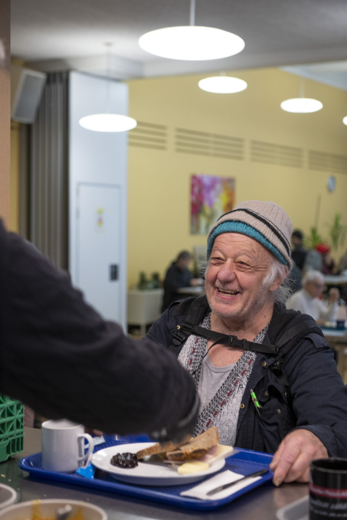 DSC4882 Ein älterer Mann lacht fröhlich in einer Cafeteria.