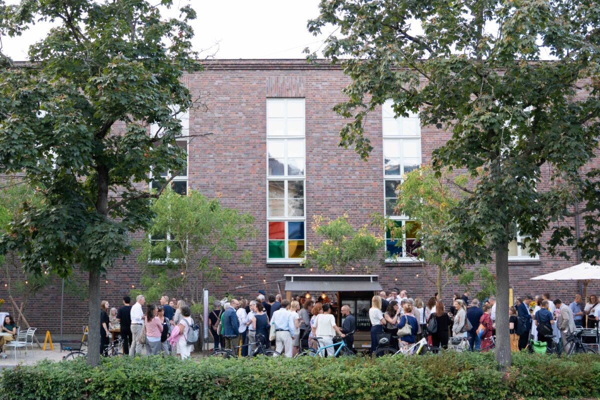 GI-beider Basel Eine Gruppe von Menschen steht vor einem Backsteingebäude und unterhält sich.