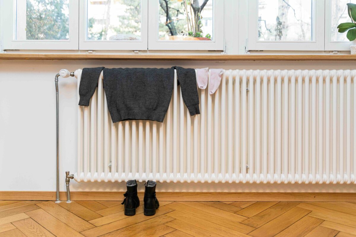 Kleidung und Stiefel trocknen an einem Heizkörper unter einem Fenster.