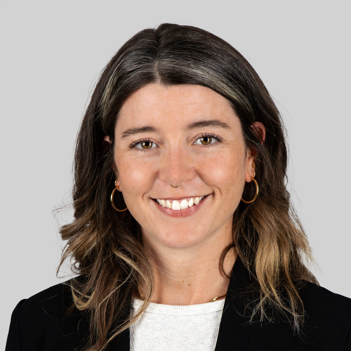 Emilie Dunn Eine lächelnde Frau mit langen Haaren und goldenen Ohrringen.