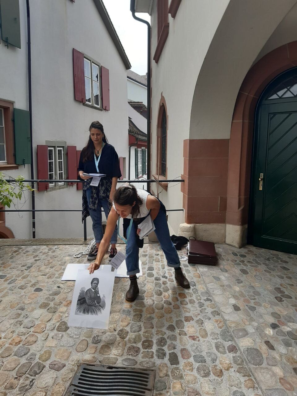 Zwei Personen untersuchen ein Foto auf einem Kopfsteinpflasterhof.