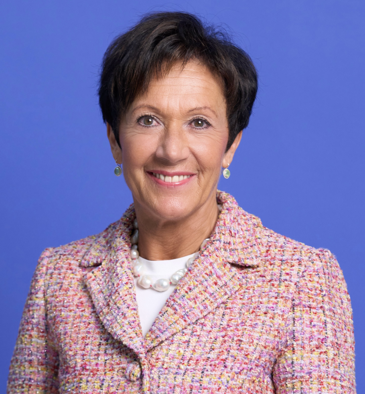 Nicole Strahm Lavanchy Eine lächelnde Frau mit kurzem Haar in einem bunten Blazer vor blauem Hintergrund.