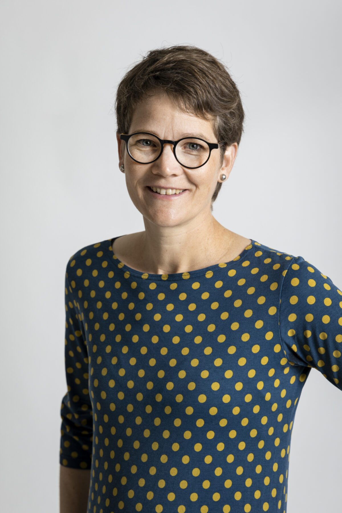 Lisa mathys 1 Eine lächelnde Frau mit kurzen Haaren und Polka-Dot-Shirt trägt eine Brille.